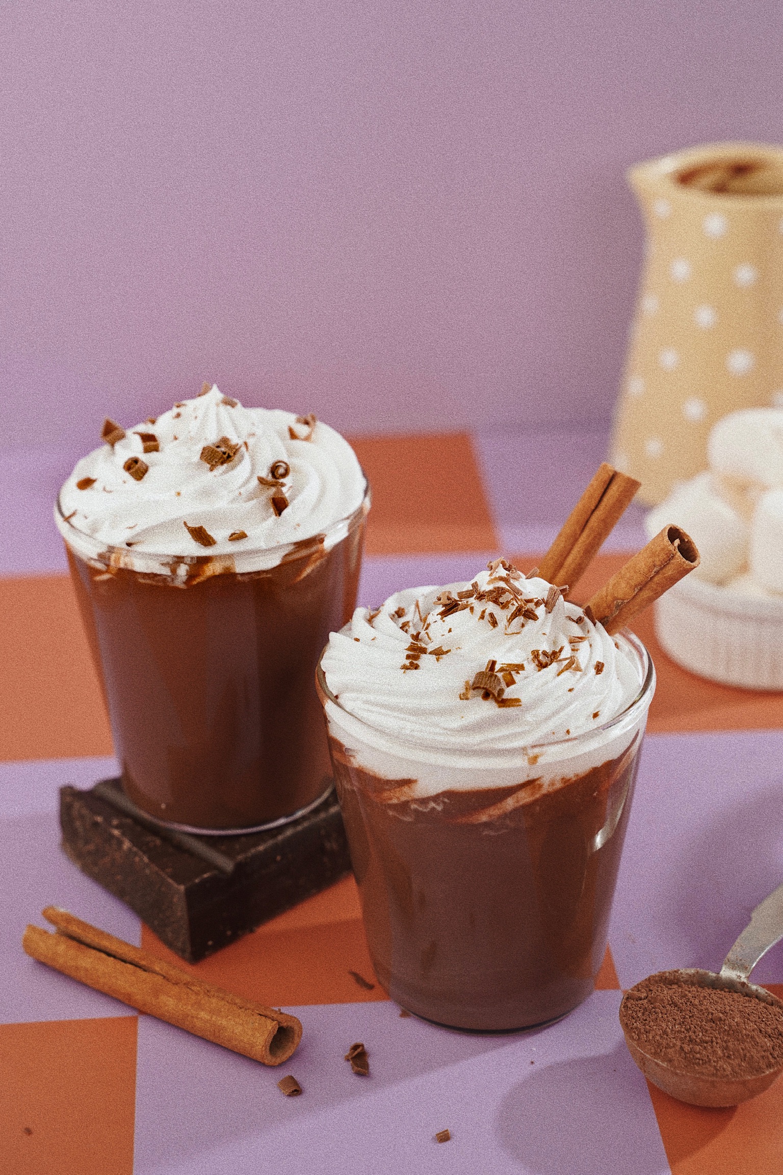 Two mugs of hot chocolate topped with whipped cream, chocolate shavings and cinnamon